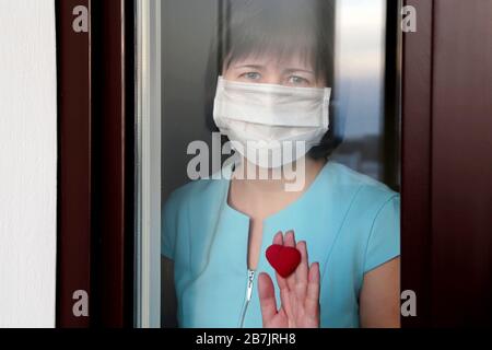 Coronavirus Quarantäne während der COVID-19-Epidemie. Traurige Frau in einer medizinischen Maske blickt aus dem Fenster Stockfoto