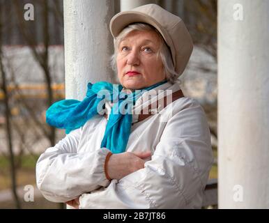 Eine elegante ältere Frau in einem modischen Liegeplatz lehnt sich an eine Säule in einem öffentlichen Park an. Stockfoto