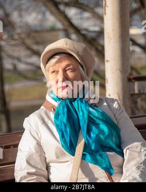 Eine elegante ältere Frau in einem modischen Liegeplatz lehnt sich an eine Säule in einem öffentlichen Park an. Stockfoto