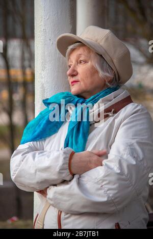 Eine elegante ältere Frau in einem modischen Liegeplatz lehnt sich an eine Säule in einem öffentlichen Park an. Stockfoto