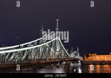 BUDAPEST, UNGARN - 10. FEBRUAR 2020: Nächtlicher Blick auf die Freiheitsbrücke (Szabadsag HID) über die Donau mit der Corvinus-Universität Stockfoto