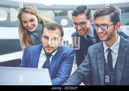 Gruppe junger Geschäftsleute arbeiten und kommunizieren, während Sie im Büro Schreibtisch sitzen zusammen mit Kollegen im Hintergrund sitzen Stockfoto