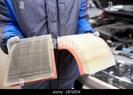 Neuer und alter verschmutzter Luftfilter für Automobilmotoren in den Händen eines Automechanikers. Auto-Reparaturkonzept. Stockfoto