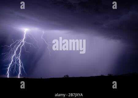 Ein heller Blitz aus Wolken erhellt einen Berg, während ein starkes Gewitter starken Regen in der Nähe von Gila Bend, Arizona, fallen lässt Stockfoto