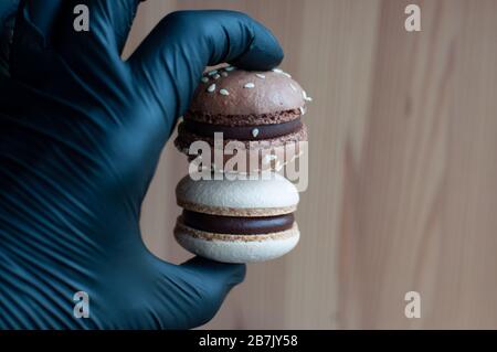 Hand in schwarzen Handschuhen halten zwei Makronen mit Schokoladenganache und Sesamsamen Stockfoto