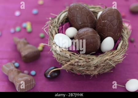 Osterbonbons auf pinkfarbenem Tisch. Vogelnest mit Schokoladeneiern und Schokoladengroschen Stockfoto