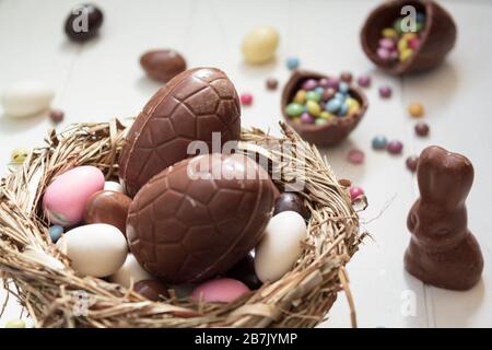Köstliche Schokoladeneier und ostermonde auf dem Gelege, Schokoladenbrötchen und Süßigkeiten auf weißem Holztisch Stockfoto