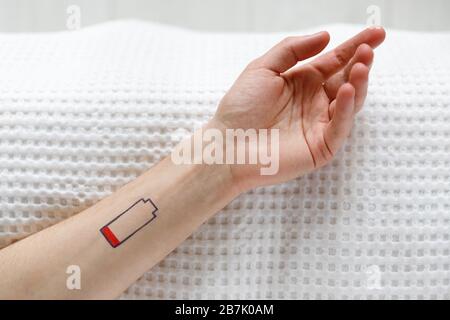 Symbol für niedrigen Batteriestand auf der menschlichen Hand. Müde Mann auf dem Bett liegend, Draufsicht. Überarbeit, erschöpft, Lebensenergie Konzept. Stockfoto