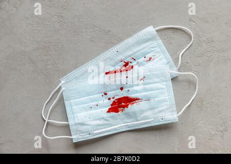 Zwei Gesichtsmasken mit Hustenblut, Draufsicht, konkretem Hintergrund. Kopierbereich. Lungenkrebs, Tuberkulose, virale Bronchitis. Stockfoto