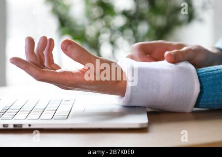 Nahaufnahme des Mannes, der eine kalte Kompression auf ein schmerzhaftes Handgelenk anwendet, das durch längere Arbeiten am Computer, Laptop, verursacht wird. Karpaltunnelsyndrom, Arthritis, neu Stockfoto