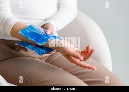 Nahaufnahme der Frau, die eine kalte Kompression auf ein schmerzhaftes Handgelenk anwendet, das durch längere Arbeit am Computer, Laptop, verursacht wird. Karpaltunnelsyndrom, Arthritis, n Stockfoto