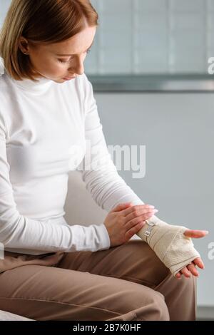 Frau, die ihr gewickeltes schmerzhaftes Handgelenk mit einem flexiblen elastischen, unterstützenden orthopädischen Verband berührt, nachdem sie Sport oder Verletzung nicht erfolgreich war, Nahaufnahme. Carpal tun Stockfoto