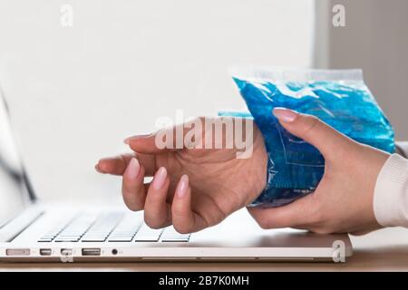 Nahaufnahme der Frau, die eine kalte Kompression auf ein schmerzhaftes Handgelenk anwendet, das durch längere Arbeit am Computer, Laptop, verursacht wird. Karpaltunnelsyndrom, Arthritis, n Stockfoto