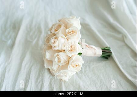 Hochzeitstrauß aus weißen, frischen, identischen Rosen auf einem zerknautschten Baumwollstoff in milchiger Farbe. Die Ansicht von oben. Platz für Text, Layout für inv Stockfoto