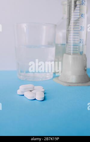 Eine Handvoll großer weißer Kapseln mit Tabletten vor dem Hintergrund von Laborgeräten, Glasgläsern und einem Becher. Stockfoto