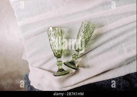 Zwei leere grüne Vintage-förmige Getränkegläser auf einer alten Tischdecke aus Baumwolle, Draufsicht, hartes Licht. Stockfoto