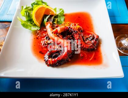 Platte mit gegrilltem Teriyake-Tintenfisch, serviert mit einem angenehmen Salat und orangefarbenem Slice garnish in einem Restaurant in Hanga Roa, Easter Island (Rapa Nui), Chile Stockfoto