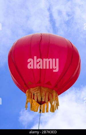 Guilin, China - 10. Mai 2010: Kleiner roter Heißluftballon mit goldenem Besatz schwebt unter blauer Wolkenlandschaft. Stockfoto