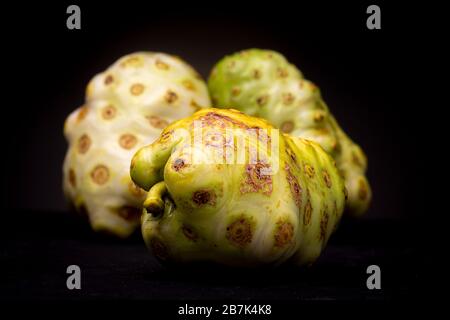 Grüne und gelbe Noni- oder Käsefrucht im Vordergrund mit zwei weiteren, einem weißen und anderen grün getönten. Studio mit niedriger Tonart und essbarem Essen Stockfoto