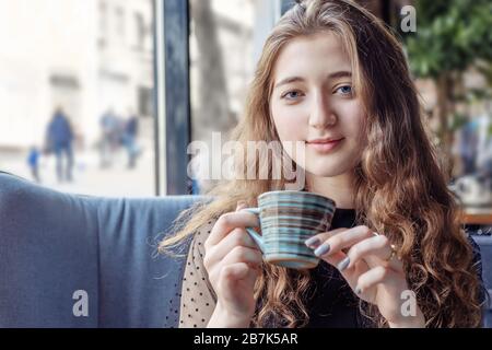 Ein rothaariges Mädchen mit einer Tasse Tee entspannt sich in einem Café. Eine lin-haarige Frau blickt in die Kamera, die einen gestreiften Becher hält Stockfoto