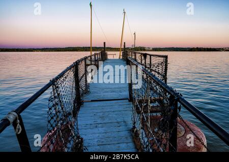 ALEXANDRIA, Virginia, USA – Ein verwittertes, wackeliges altes Dock erstreckt sich in den Potomac River an der Uferpromenade der Altstadt von Alexandria. Dieses Gebäude mit seinen abgenutzten Holzdielen und verwitterten Pfosten ist ein Zeugnis der langen maritimen Geschichte Alexandrias. Das Dock bietet einen malerischen Blick auf den Fluss, der die alte mit dem wiederbelebten Hafengebiet dieser historischen Hafenstadt kontrastiert. Stockfoto