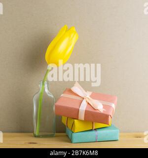 Geschenkschachteln mit gelber Tulpenblume in Glasflasche auf Holztisch mit braunem Hintergrund. Jubiläumskonzept, Blumenarrangement, Kopierraum Stockfoto