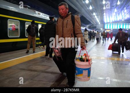 Die Passagiere tragen einen Plastikeimer, der ihr Gepäck enthält, und bereiten sich darauf vor, an Bord des Zuges zu gehen, der zu Hause am Bahnhof von Peking, Peking, China, 1 fährt Stockfoto