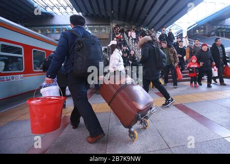 Passagiere tragen Plastikeimer, der ihr Gepäck enthält, und bereiten sich darauf vor, an Bord des Zuges zu gehen, der zu Hause am Bahnhof Beijingxi, Peking, China, fährt. Stockfoto