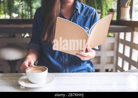 Nahaufnahme einer asiatischen Frau, die ein Buch liest, während sie Kaffee in einem modernen Café trinkt Stockfoto