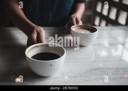 Nahaufnahme der Hände mit zwei weißen Tassen heißen Kaffees auf dem Tisch im Café Stockfoto