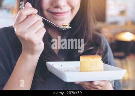 Nahaufnahme einer glücklichen Frau, die Käsekuchen mit Löffel im Café hält und genießt Stockfoto