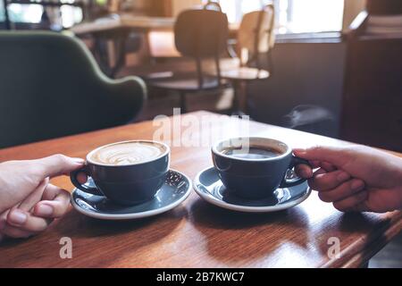 Nahaufnahme von zwei Händen, die Kaffee und heiße Schokoladenbecher auf Holztisch im Café halten Stockfoto