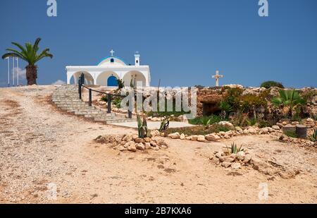 Die Panoramasicht auf die Ayia Thekla Chapel (Agia Thekla), auf die felsige Küste über dem Meer und die kleine Katakombenkirche, die in den Felsen gehauen ist. Ayia Na Stockfoto