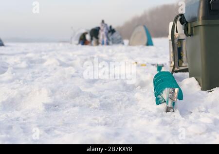 Werkzeuge und Sachen zum Winterfischen auf einem gefrorenen Teich im Schnee auf dem Hintergrund von Winterzelten Stockfoto