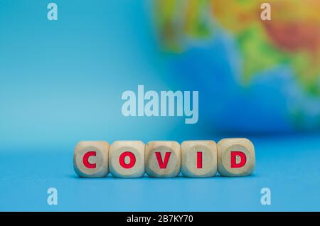 COVID-Beschriftung auf Holzwürfeln auf dem Hintergrund des Planeten Erde. Konzept einer Coronavirus-Pandemie. Stockfoto