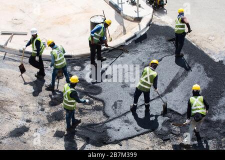 Eine Gruppe von Bauarbeitern, die schnell zusammenarbeiten, um den schwarzen Sand auf dem Boden in einem Bauprozess auszubreiten. Singapur. Stockfoto