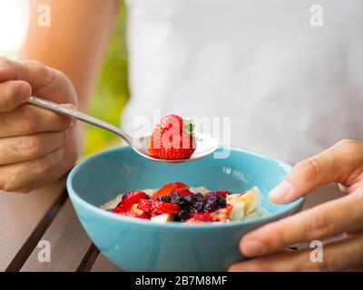 Herzförmige Erdbeere in den Händen des Menschen auf einem weißen Hemdhintergrund, die eine gesunde Ernährung oder kardiovaskuläre Gesundheit darstellt, Liebe. Stockfoto