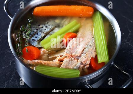 Fischbrühe oder Suppe aus Lachs, Zwiebel, Karotte, Sellerie, Kräutern und Gewürzen in einem Vorratsbehälter auf einem Betontisch, in der Nähe Stockfoto
