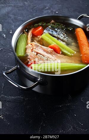 Langsam gekochte Fischbrühe oder Suppe aus Lachs, Zwiebel, Karotte, Sellerie, Kräutern und Gewürzen in einem Stocktopf auf einem Betontisch, vertikale Ansicht von oben Stockfoto