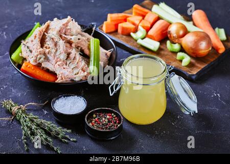Nahaufnahme von langsam gekochtem Fischbrühe oder Lachsbestand in einem Glasbecher auf einem Betontisch mit Fischfleisch, Knochen und Gemüse in einer Schüssel Stockfoto