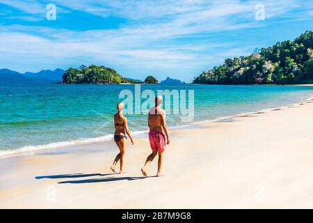 Mann und Frau, die am Strand von Andaman, der Bucht von Datai an der Meerenge von Malaca, der Andamanensee mit der Insel Palau Anak Datai am Horizont, Langkawi, Malaysia, spazieren gehen Stockfoto