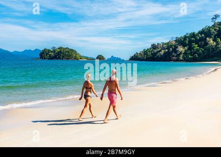 Mann und Frau, die am Strand von Andaman, der Bucht von Datai an der Meerenge von Malaca, der Andamanensee mit der Insel Palau Anak Datai am Horizont, Langkawi, Malaysia, spazieren gehen Stockfoto