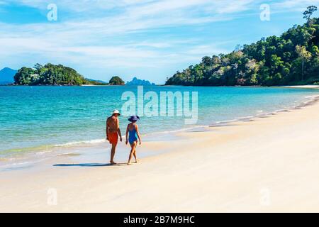 Mann und Frau, die am Strand von Andaman, der Bucht von Datai an der Meerenge von Malaca, der Andamanensee mit der Insel Palau Anak Datai am Horizont, Langkawi, Malaysia, spazieren gehen Stockfoto