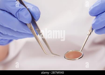 Nahaufnahme der Zahnarzthandschuhe in blauen Latexhandschuhen mit Pinzette und Mundspiegel. Geringe Schärfentiefe. Konzept für medizinische Hilfsmittel. Stockfoto