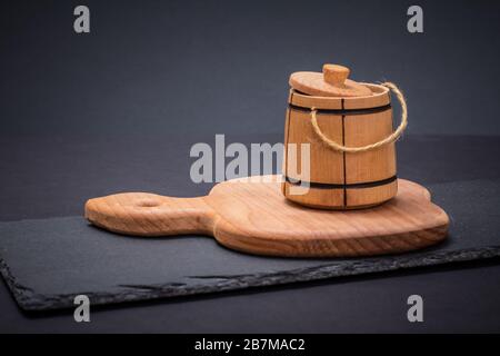 Kleines Fass zum Aufbewahren von Salz oder Gewürzen auf Holz- und Steinschneideplatten in schwarzem Hintergrund. Stockfoto