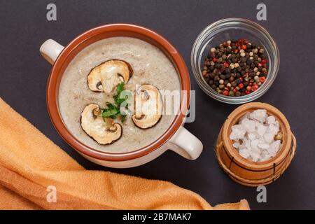 Leckere hausgemachte Pilzcremesuppe mit Champignons in Porzellanschale, allspices und kleinem Holzfass mit Salz auf schwarzem Steinbrett. Top VI Stockfoto