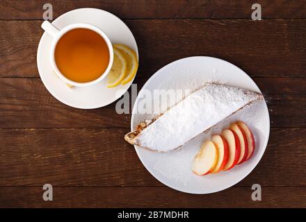 Strudel mit Äpfeln und einer Tasse Tee mit Zitrone auf einem Holzbrett Stockfoto