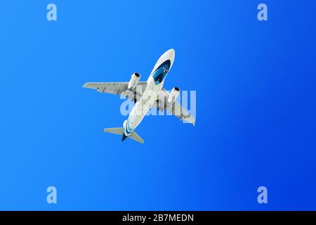 Weißes Flugzeug fliegt auf hellblauem Himmel Nahaufnahme, Passagierflugzeug Start, Flugbanner, Reiseplaster, Urlaubskonzept, Copy-Space Stockfoto
