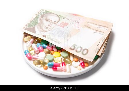 Pillen und ukrainisches Geld auf weißem Hintergrund. Das Konzept des Preisanstiegs bei Drogen. Stockfoto