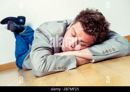 Unterhaltsames Porträt eines freiberuflichen Mitarbeiters, der auf dem Boden liegt und zu Hause auf dem Parkett schläft Stockfoto